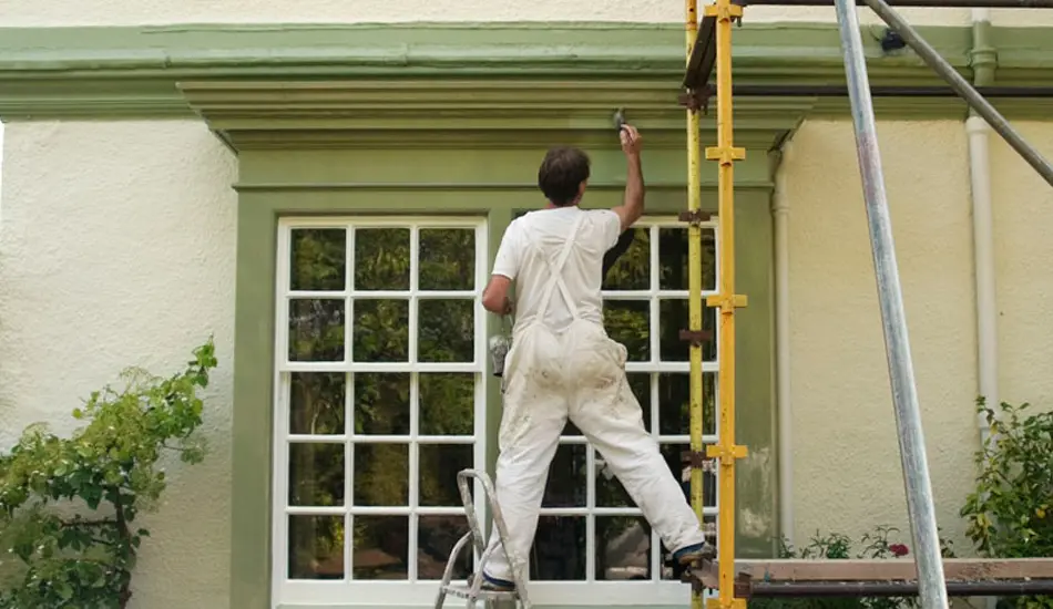 Pintor trabajando en la fachada de una casa con ventanas en madera